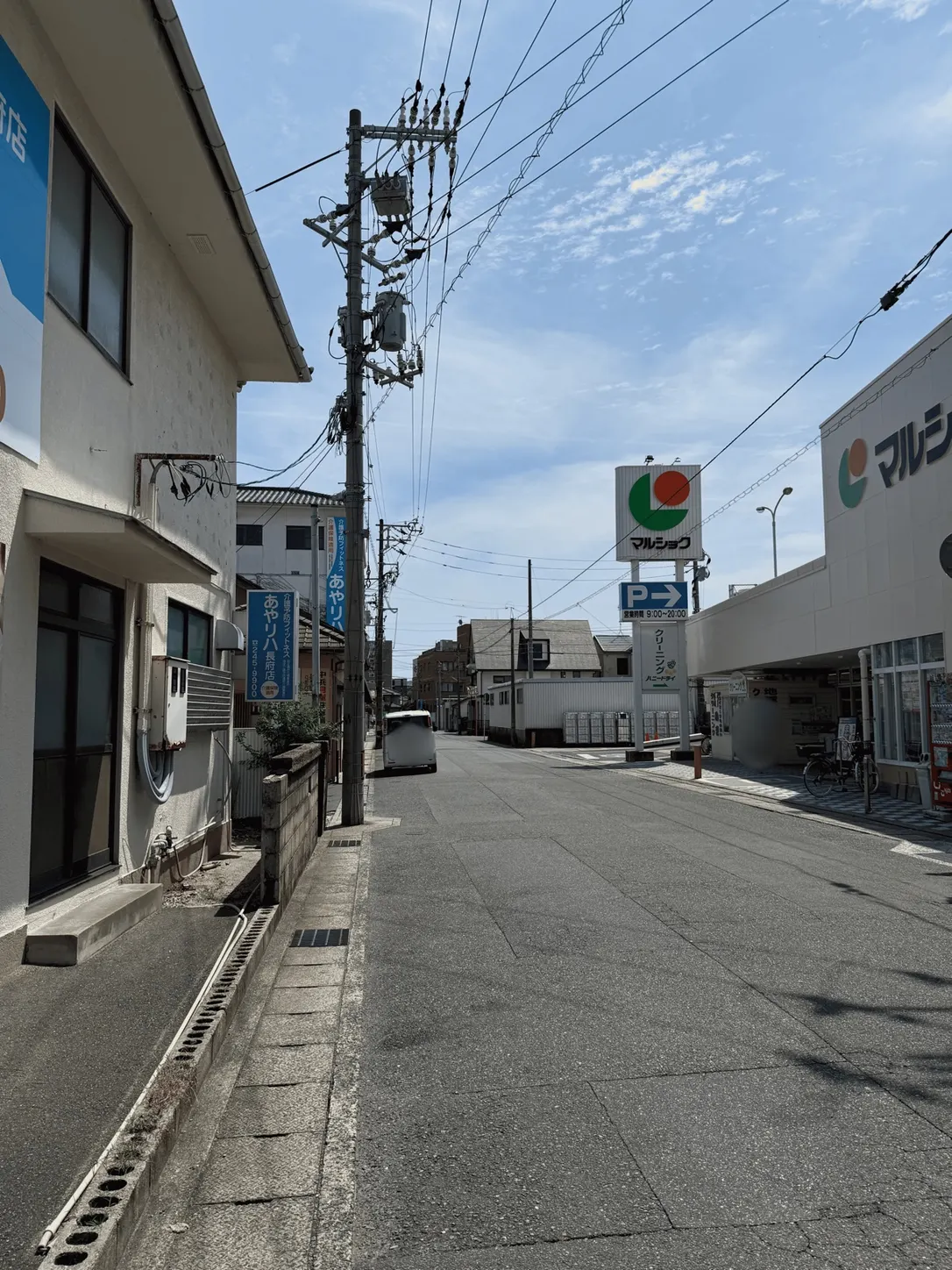 通り沿いから見たマルショク長府店。手前に青い「P」と右向き矢印の駐車場案内看板が立っている。